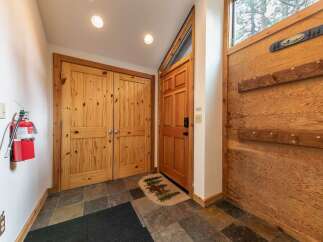 Step into a warm and inviting entryway featuring rustic knotty pine double doors and a charming wooden front door with a decorative moose and pine tree mat.