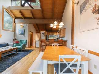 Experience rustic charm in this open-concept living and dining area, featuring a vaulted wood-beam ceiling and a cozy fireplace.