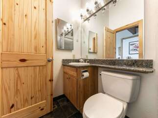 This charming bathroom features a rustic wooden door and vanity, complemented by a granite countertop and a modern stainless steel light fixture.