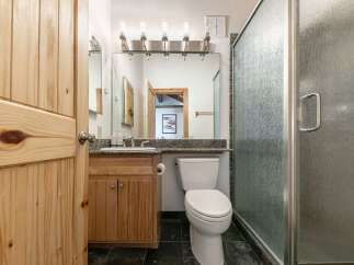 This charming bathroom features a rustic wooden door and vanity, complemented by a granite countertop and a modern glass shower enclosure.