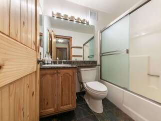 This charming bathroom features a rustic wooden vanity with a granite countertop, complemented by a modern toilet and a sleek glass-enclosed shower.