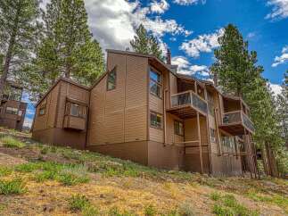 Nestled amongst tall pine trees, this multi-level brown wood-sided home offers a unique architectural design with multiple balconies and large windows.