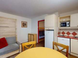 This studio apartment offers a compact yet functional living space, featuring a comfortable sofa with red accent pillows and a dining area with a yellow table and wooden chairs.