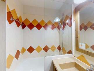 This charming bathroom features a vibrant tiled shower enclosure with a diamond pattern in warm orange and yellow hues.