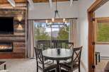Experience cozy mountain living in this charming dining area, featuring a rustic wood-paneled accent wall with a modern fireplace and a large window offering breathtaking views of the surrounding landscape.