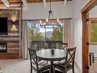 Experience cozy mountain living in this charming dining area, featuring a rustic wood-paneled accent wall with a modern fireplace and a large window offering breathtaking views of the surrounding landscape.