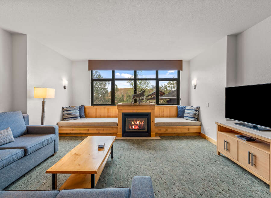Cozy up by the fireplace in this inviting living room, featuring a built-in wooden bench seating area perfect for enjoying the scenic views through the large window.