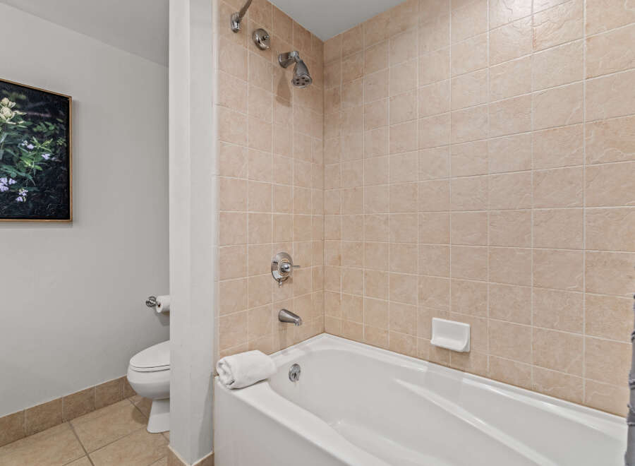 This bathroom features a clean and functional design with a white bathtub and shower combination, complemented by neutral-toned tiled walls.