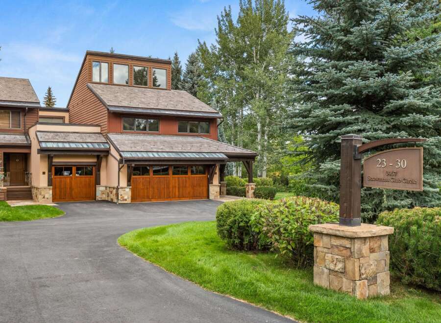 This stunning mountain residence features a warm, wood-accented exterior with multiple garage doors and a welcoming entryway.