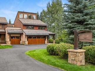 This stunning mountain residence features a warm, wood-accented exterior with multiple garage doors and a welcoming entryway.