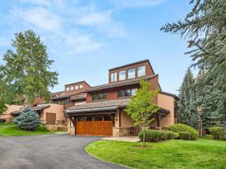 Discover this stunning mountain home featuring a warm, natural wood garage door and a charming stone facade.
