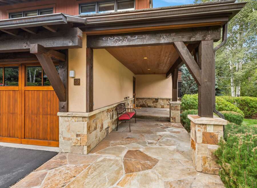 Experience rustic charm with this inviting covered entryway, featuring exposed wooden beams and a natural stone facade.