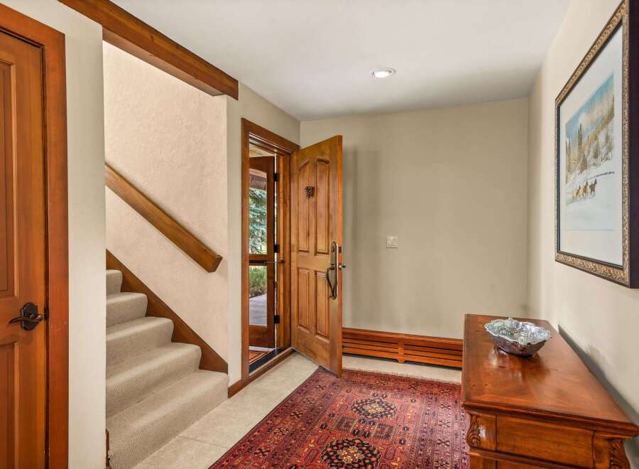 Step into this inviting entryway featuring a warm wooden door and a plush oriental rug that leads to a carpeted staircase.