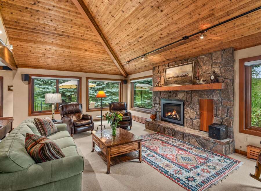 Experience rustic charm in this inviting living room, featuring a grand stone fireplace and a vaulted wood-paneled ceiling.