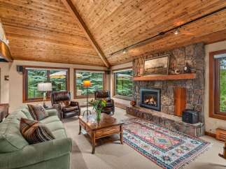 Experience rustic charm in this inviting living room, featuring a grand stone fireplace and a vaulted wood-paneled ceiling.