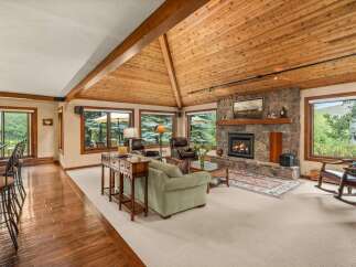 Experience rustic charm in this spacious living area, featuring a grand stone fireplace and a vaulted, wood-paneled ceiling.