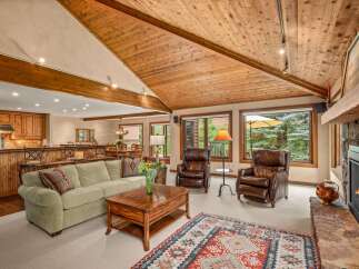 Experience rustic charm and modern comfort in this inviting living space, featuring a vaulted wood-paneled ceiling and a cozy stone fireplace.
