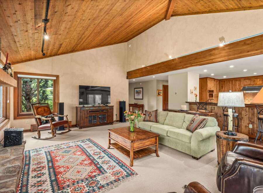 Experience rustic charm in this spacious living area featuring a vaulted wood-paneled ceiling and a cozy stone fireplace.