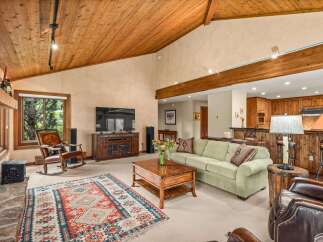 Experience rustic charm in this spacious living area featuring a vaulted wood-paneled ceiling and a cozy stone fireplace.