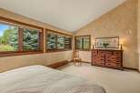 Experience serene mountain living in this charming bedroom, featuring a vaulted ceiling and large windows that frame breathtaking views of lush evergreen trees.
