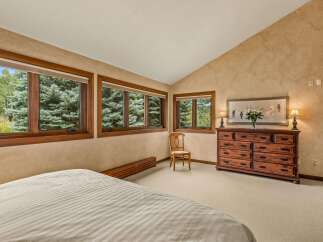 Experience serene mountain living in this charming bedroom, featuring a vaulted ceiling and large windows that frame breathtaking views of lush evergreen trees.