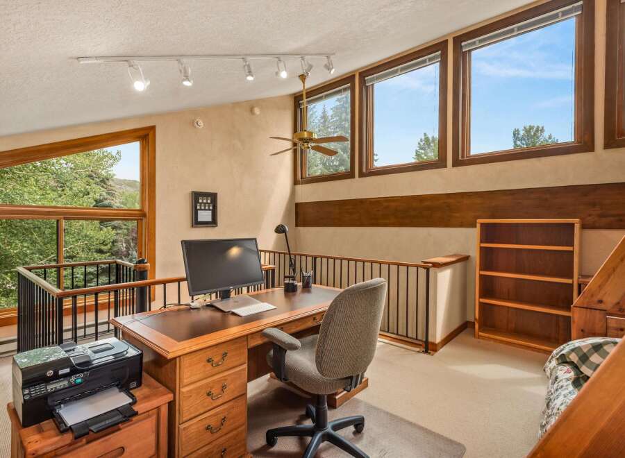 This spacious loft office features a large wooden desk with a computer, printer, and ample storage, perfect for a home workspace.
