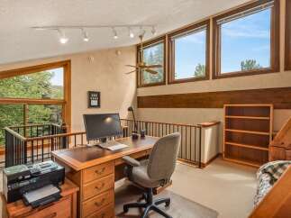 This spacious loft office features a large wooden desk with a computer, printer, and ample storage, perfect for a home workspace.