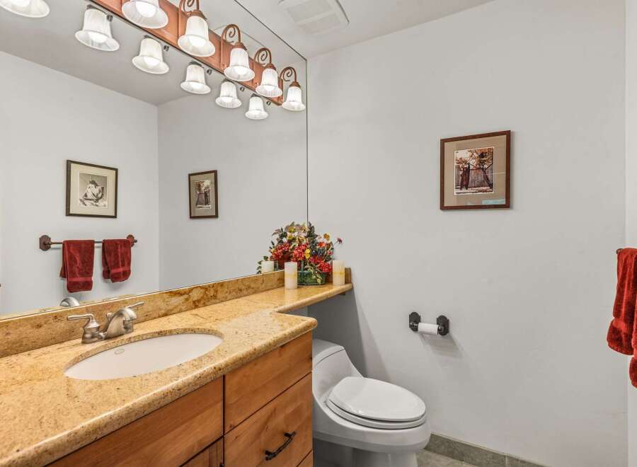 This charming bathroom features a granite-topped vanity with a single sink and ample storage, complemented by a large mirror with an overhead light fixture.