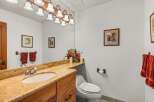 This charming bathroom features a granite-topped vanity with a single sink and ample storage, complemented by a large mirror with an overhead light fixture.