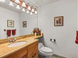 This charming bathroom features a granite-topped vanity with a single sink and ample storage, complemented by a large mirror with an overhead light fixture.