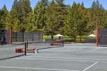 Enjoy a game of tennis on this pristine court, surrounded by lush green trees and a clear blue sky.