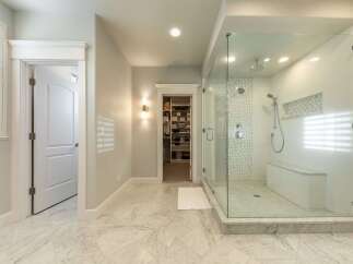 Experience luxury in this master bathroom featuring a spacious walk-in shower with a built-in bench and intricate tile accents.