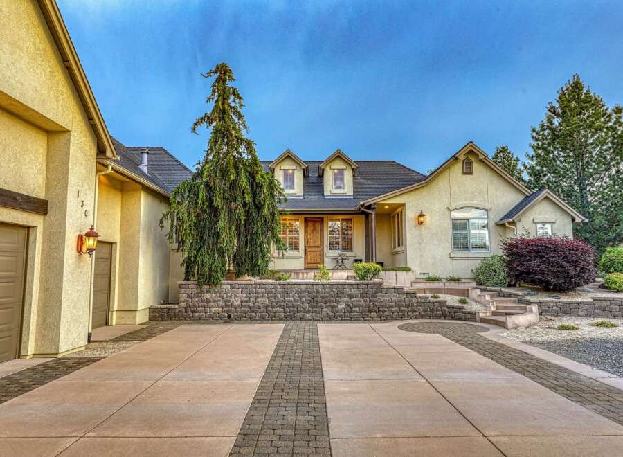 Discover this stunning stucco home featuring a welcoming driveway with decorative brick accents and a charming stone retaining wall.