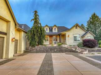 Discover this stunning stucco home featuring a welcoming driveway with decorative brick accents and a charming stone retaining wall.