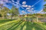 Experience serene country living with this picturesque property, featuring a charming yellow house nestled amidst lush greenery and rolling hills.