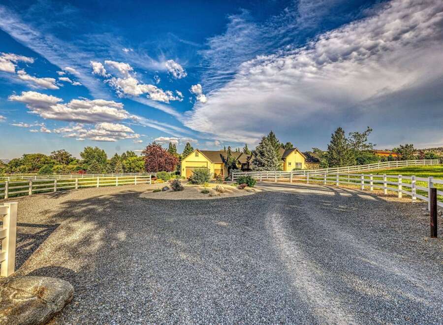 Discover this charming yellow home nestled on a sprawling property, complete with a picturesque white fence and a long gravel driveway.