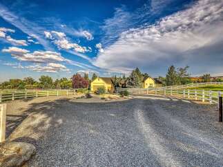 Discover this charming yellow home nestled on a sprawling property, complete with a picturesque white fence and a long gravel driveway.