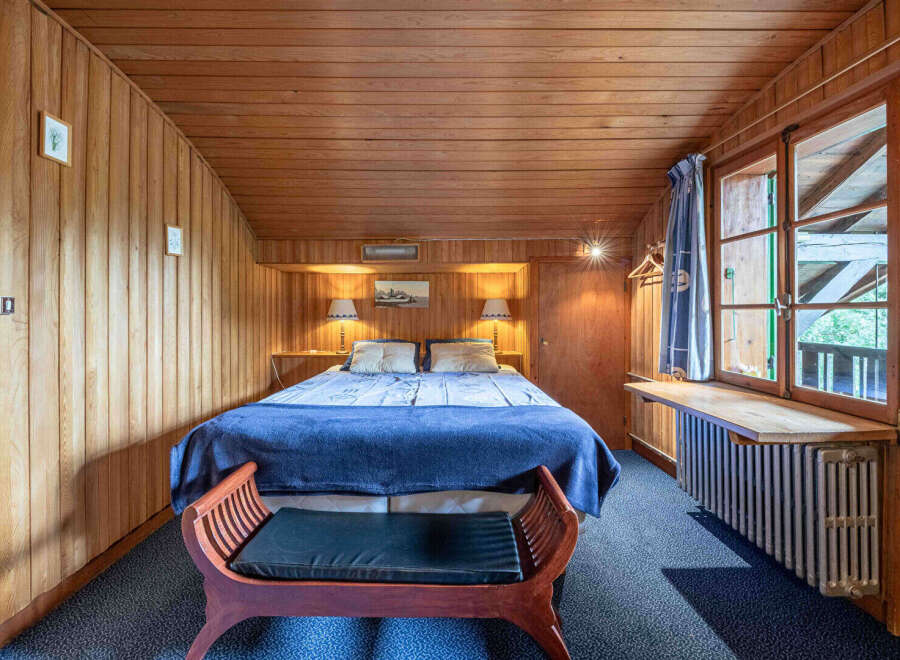 Experience cozy comfort in this charming wood-paneled bedroom, featuring a plush queen-sized bed adorned with a deep blue comforter and matching pillows.