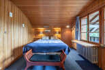 Experience cozy comfort in this charming wood-paneled bedroom, featuring a plush queen-sized bed adorned with a deep blue comforter and matching pillows.