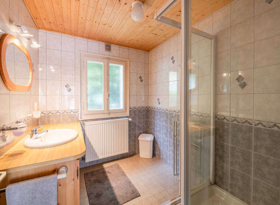 This charming bathroom features a wooden vanity with a white sink and a sleek chrome faucet, complemented by a large oval mirror with a wooden frame.