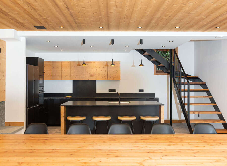 Experience modern living in this stunning kitchen and dining area, featuring a sleek black island with bar stools and a warm wooden ceiling.