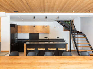 Experience modern living in this stunning kitchen and dining area, featuring a sleek black island with bar stools and a warm wooden ceiling.