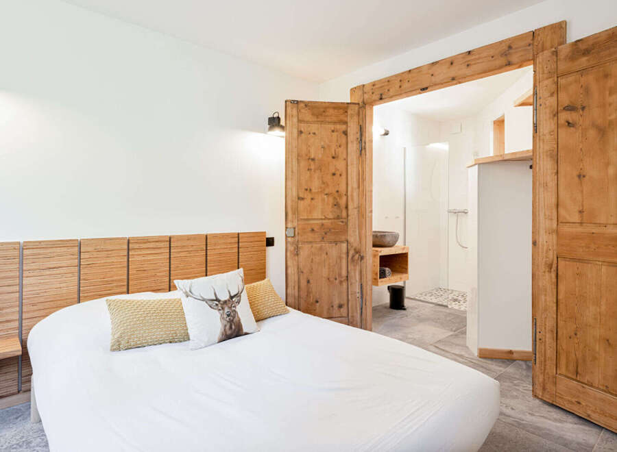 Experience rustic charm in this inviting bedroom featuring a unique wooden headboard and a comfortable bed adorned with decorative pillows, including one with a striking deer motif.
