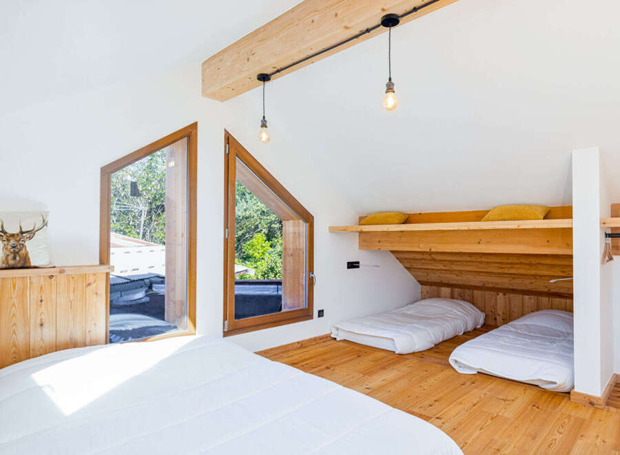 Discover this charming attic bedroom featuring unique triangular windows that offer picturesque views of the surrounding greenery.