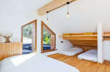Discover this charming attic bedroom featuring unique triangular windows that offer picturesque views of the surrounding greenery.