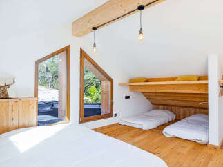 Discover this charming attic bedroom featuring unique triangular windows that offer picturesque views of the surrounding greenery.