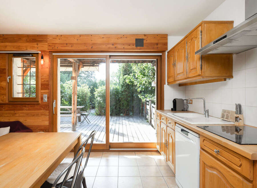This charming kitchen features warm wooden cabinetry and a spacious dining area with a large sliding glass door that opens to a beautiful wooden deck and lush greenery.