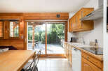 This charming kitchen features warm wooden cabinetry and a spacious dining area with a large sliding glass door that opens to a beautiful wooden deck and lush greenery.