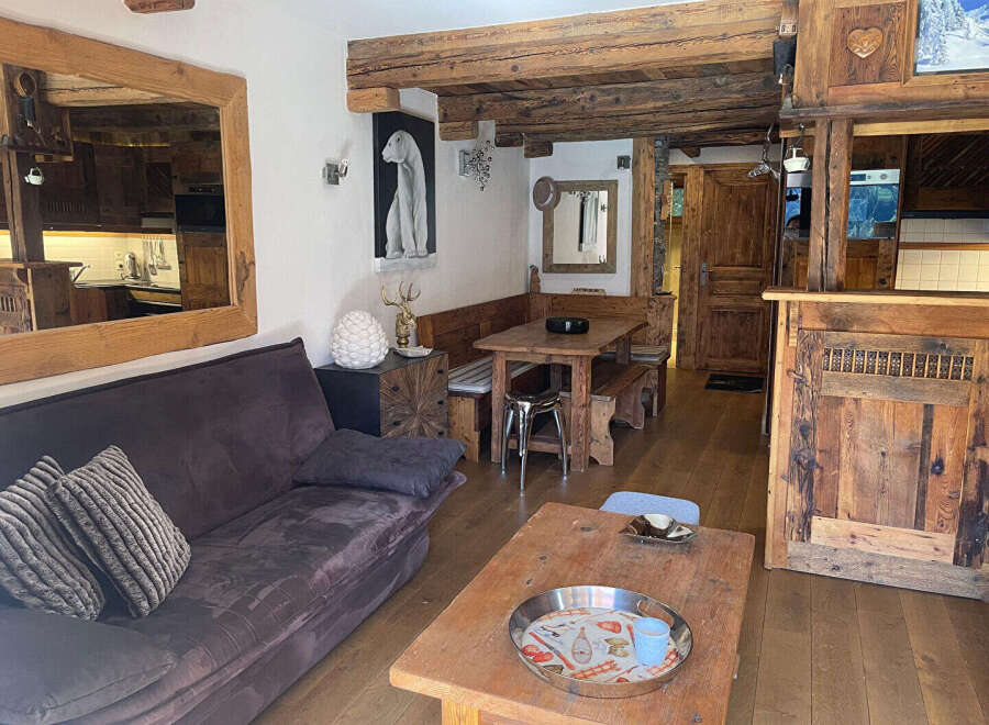 Experience rustic charm in this cozy living space featuring a plush sofa, a traditional wooden dining set, and exposed wooden beams that enhance the alpine ambiance.