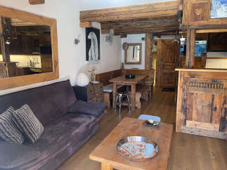 Experience rustic charm in this cozy living space featuring a plush sofa, a traditional wooden dining set, and exposed wooden beams that enhance the alpine ambiance.